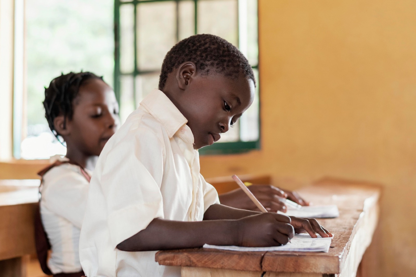 Two pupils writing side by side in a classroom